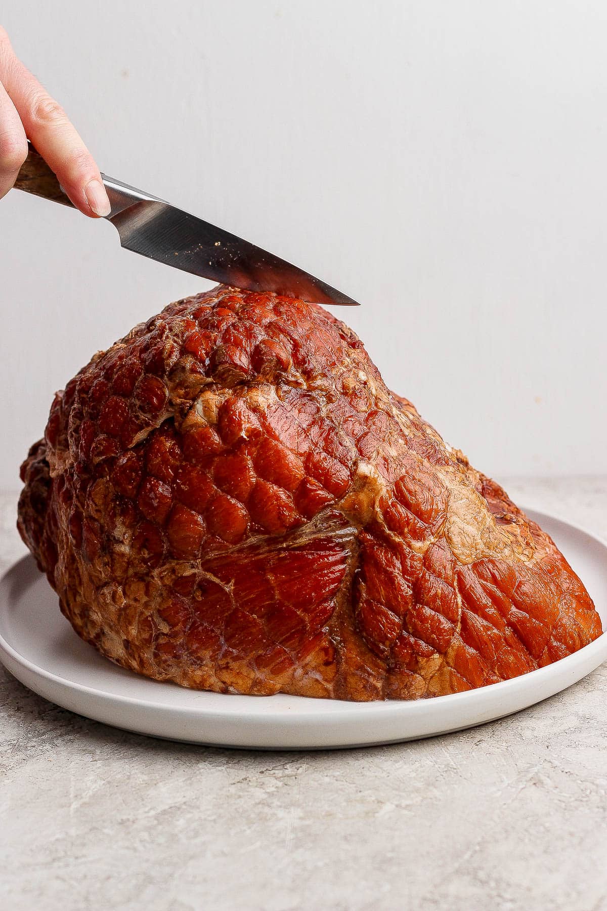 A bone-in ham on a large plate being scored by a paring knife.