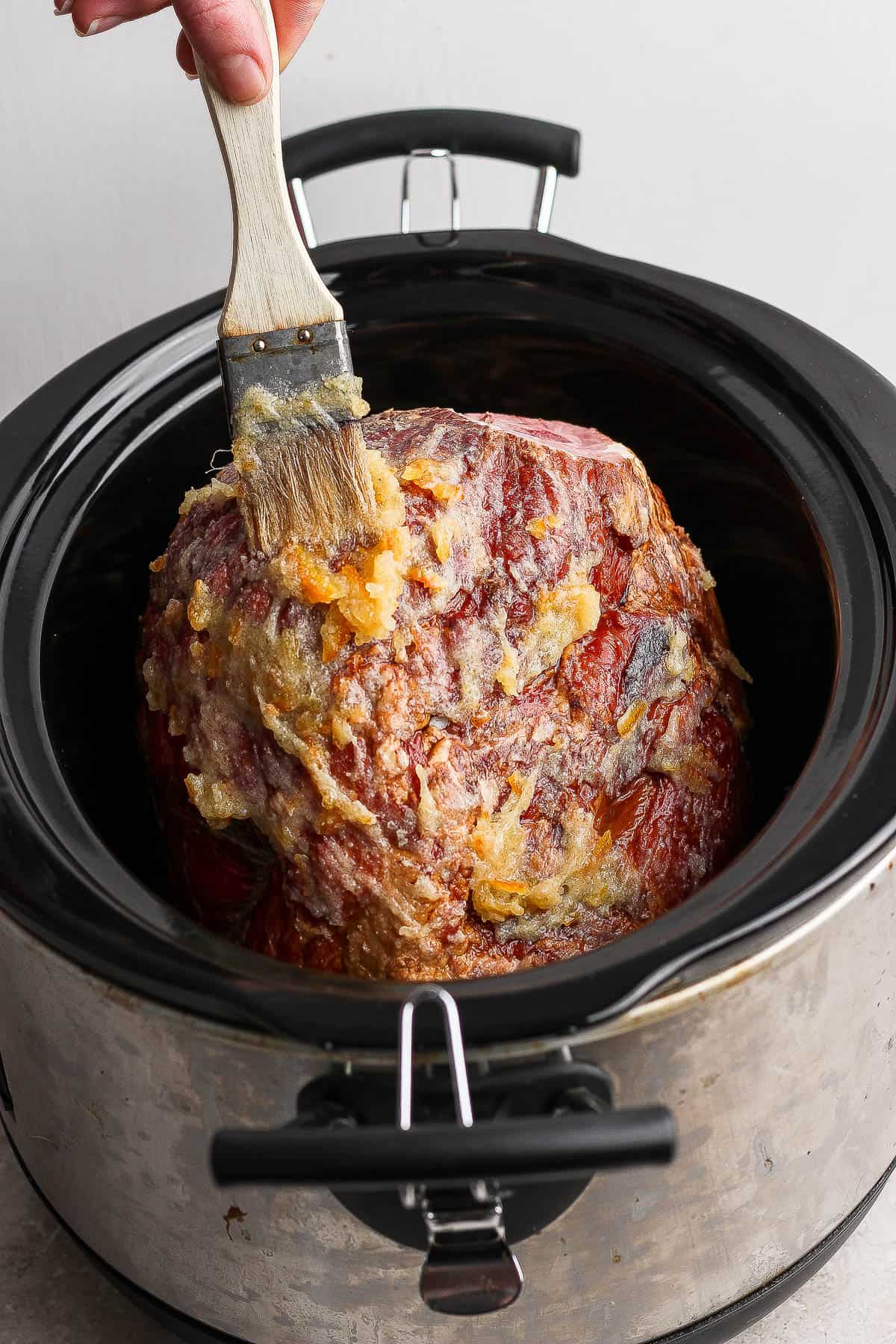 An orange glazed ham in a crockpot with the orange glaze being brushed on.