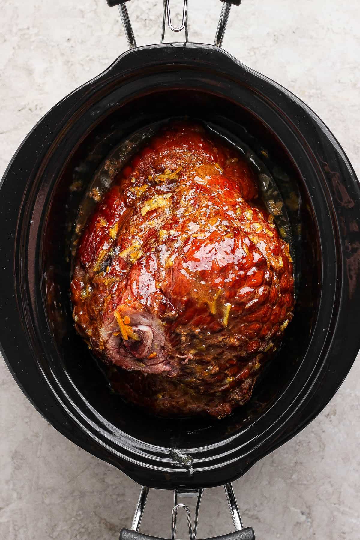 A fully cooked orange glazed ham in the slow cooker.