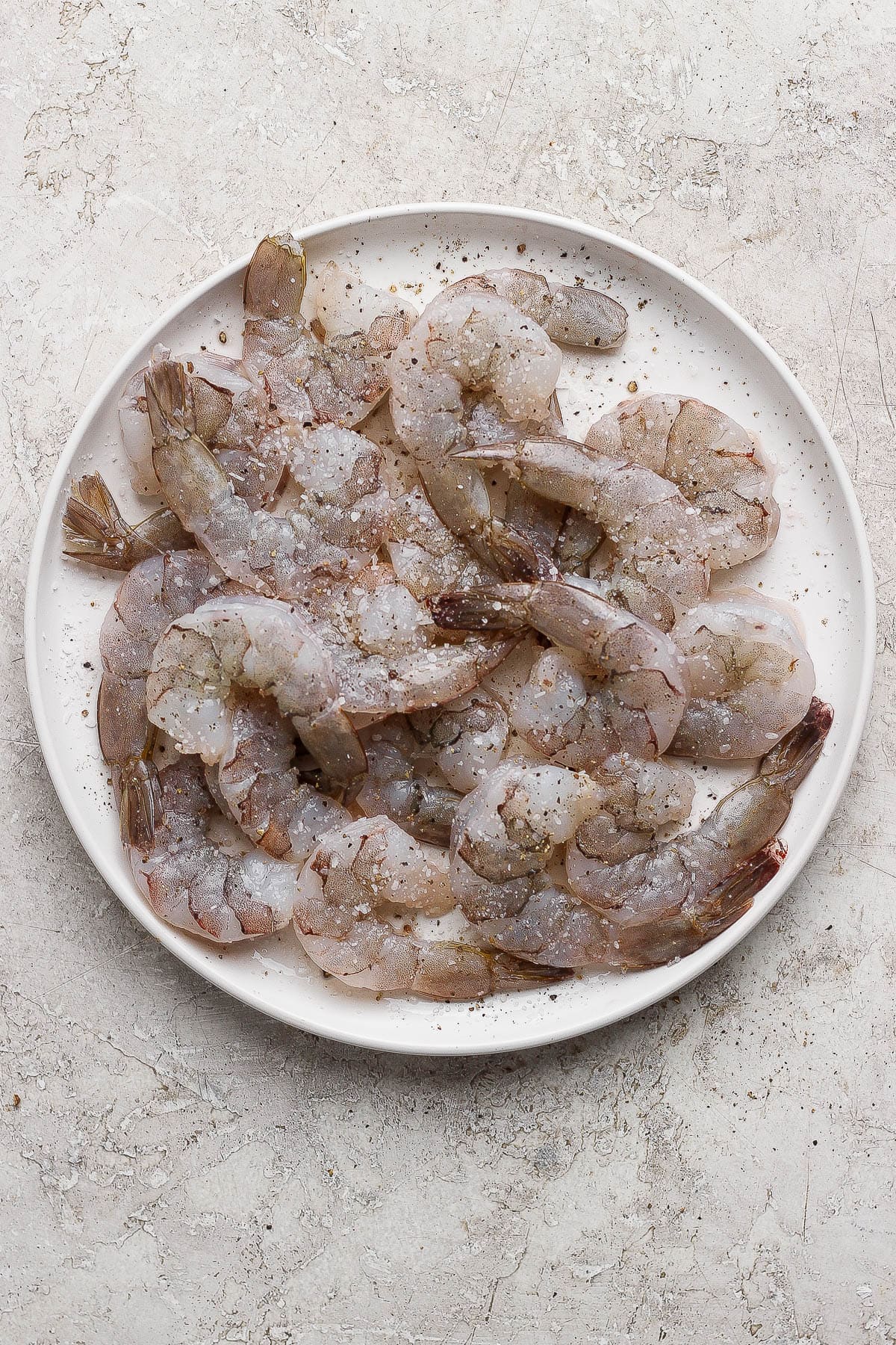 Raw shrimp on a plate with salt and pepper.