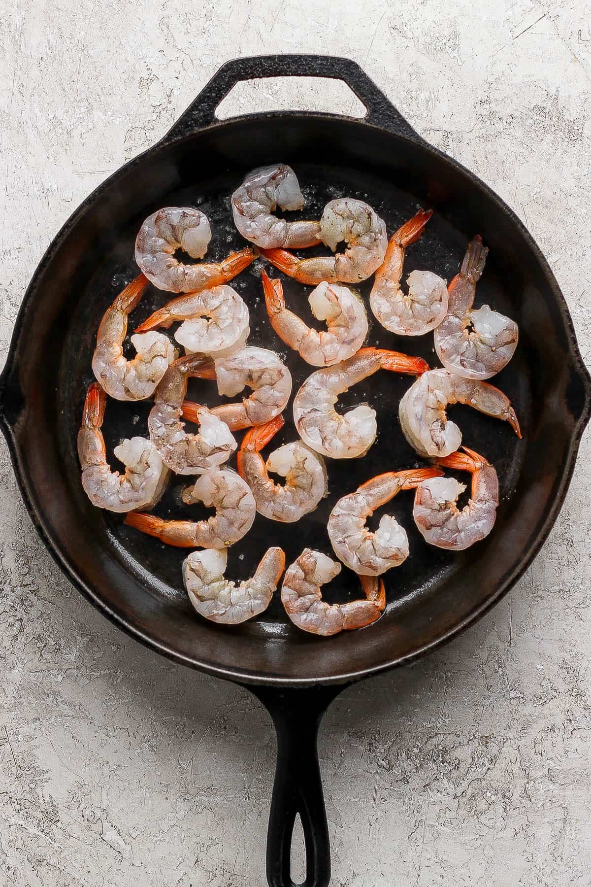 Pan fried shrimp cooking in a cast iron skillet before being flipped over.