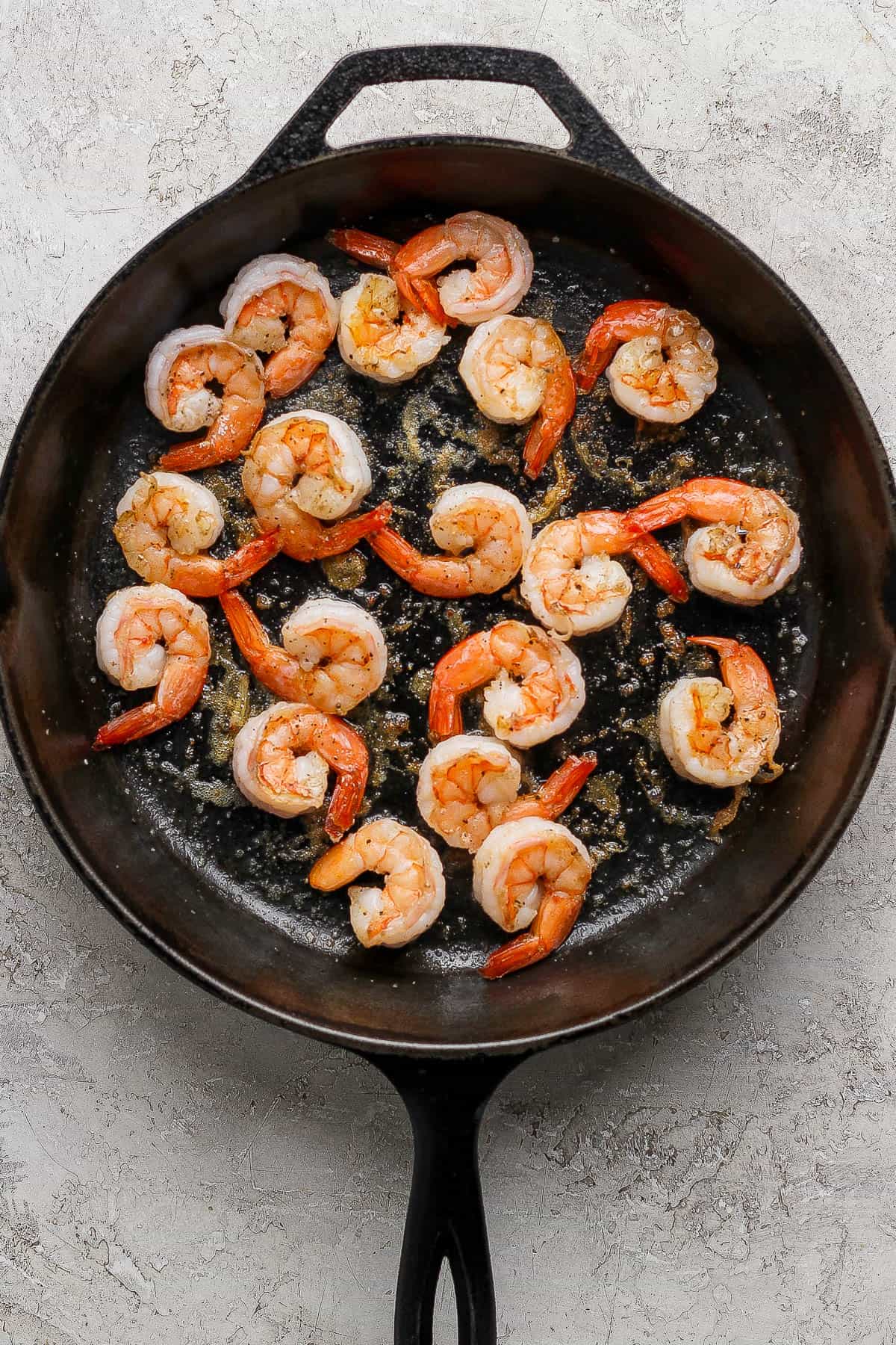 Several fully cooked pan fried shrimp in a cast iron skillet.