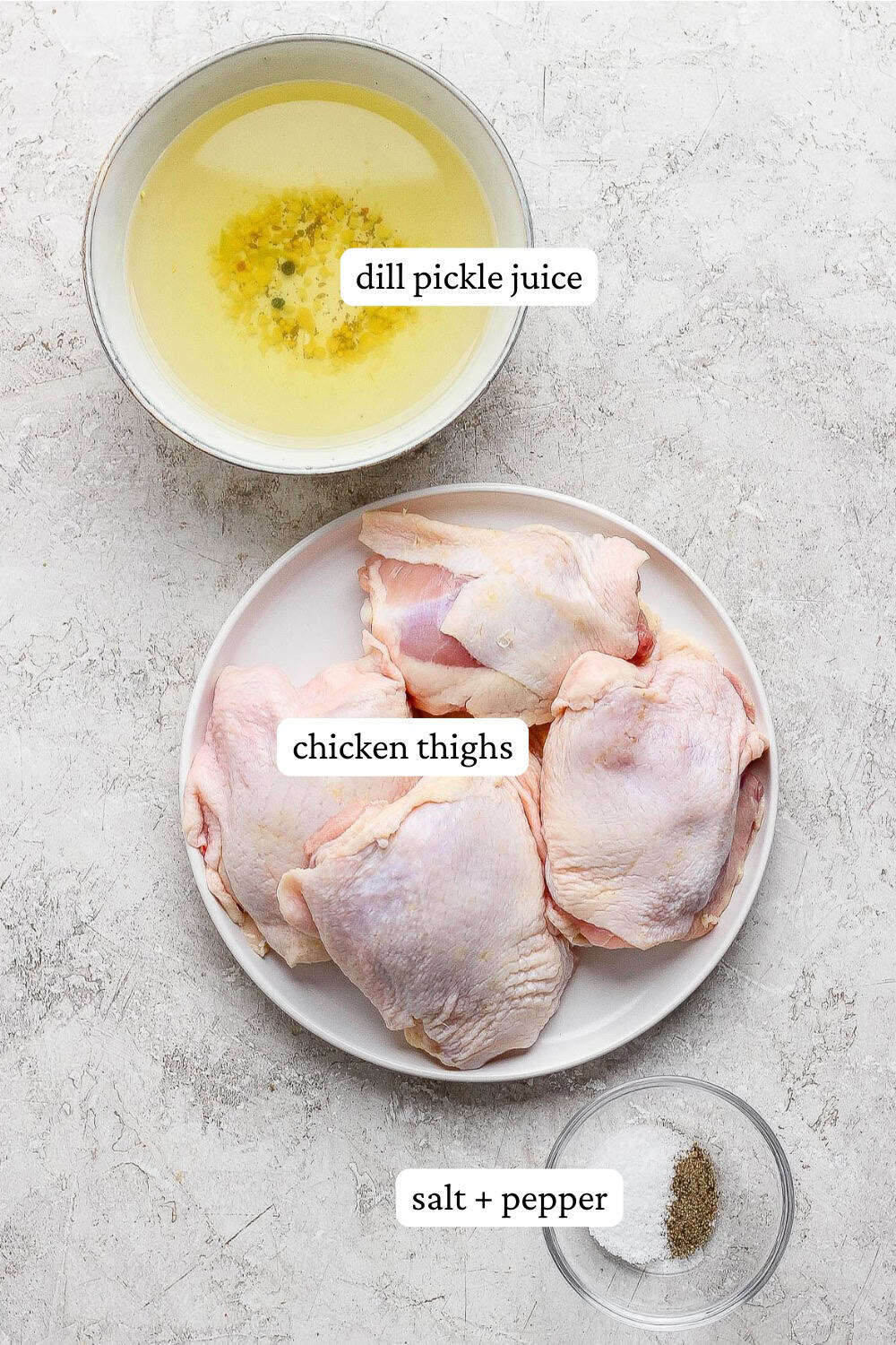 Raw chicken thighs on a plate next to a bowl of pickle juice and small bowl of salt and pepper.