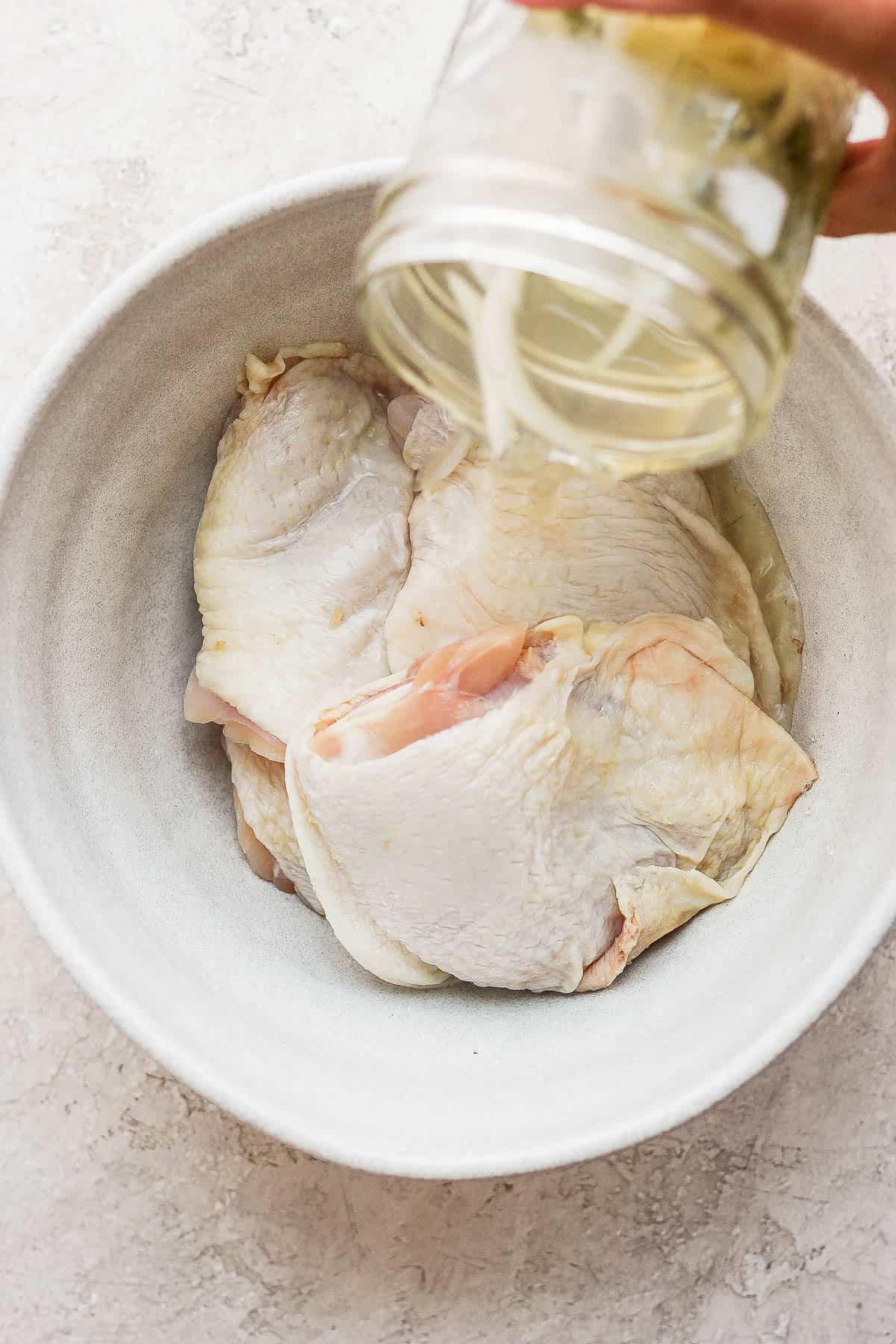 Dill pickle juice being poured over chicken thighs in a bowl.