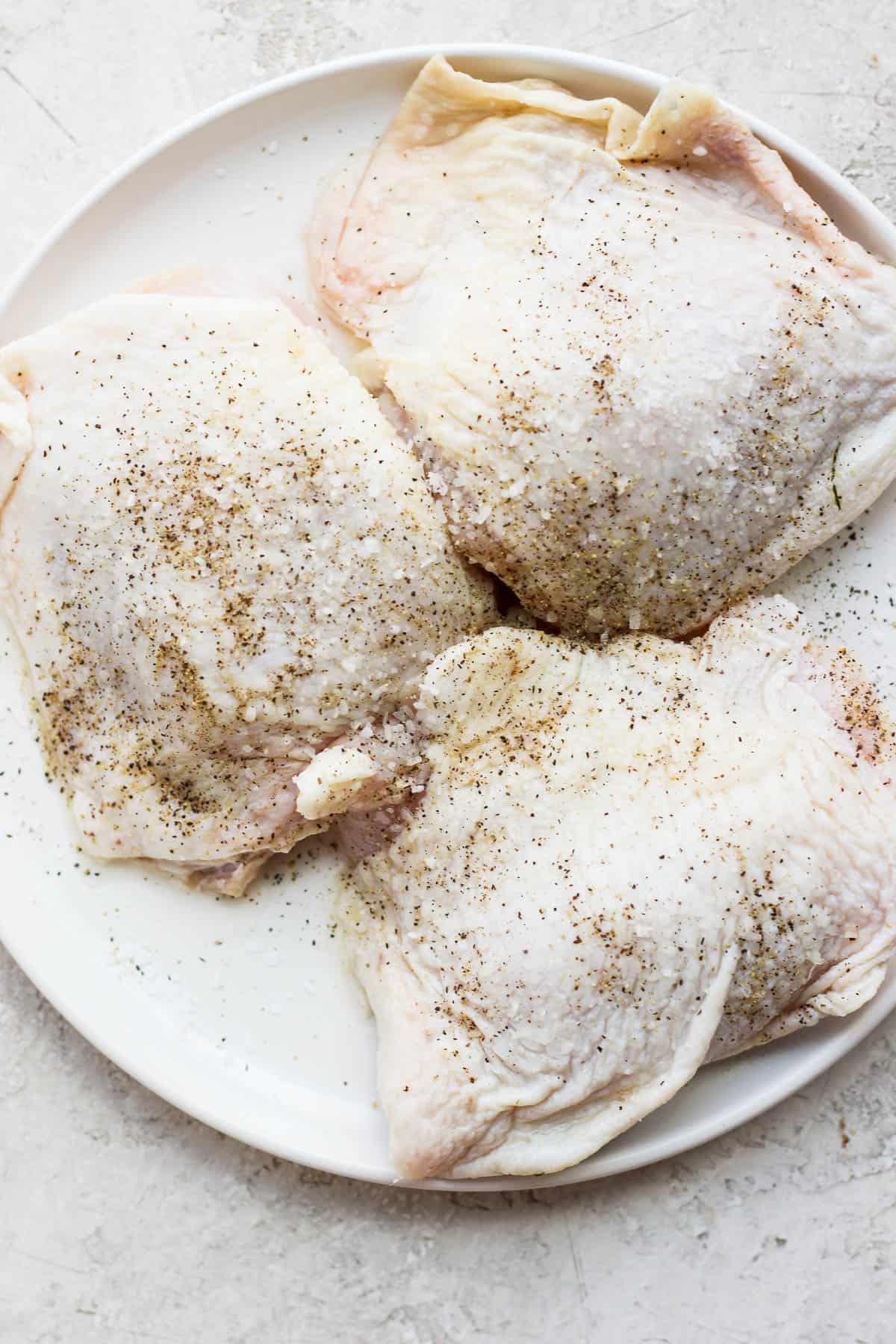 Pickle brine chicken thighs seasoned with salt and pepper on a white plate.