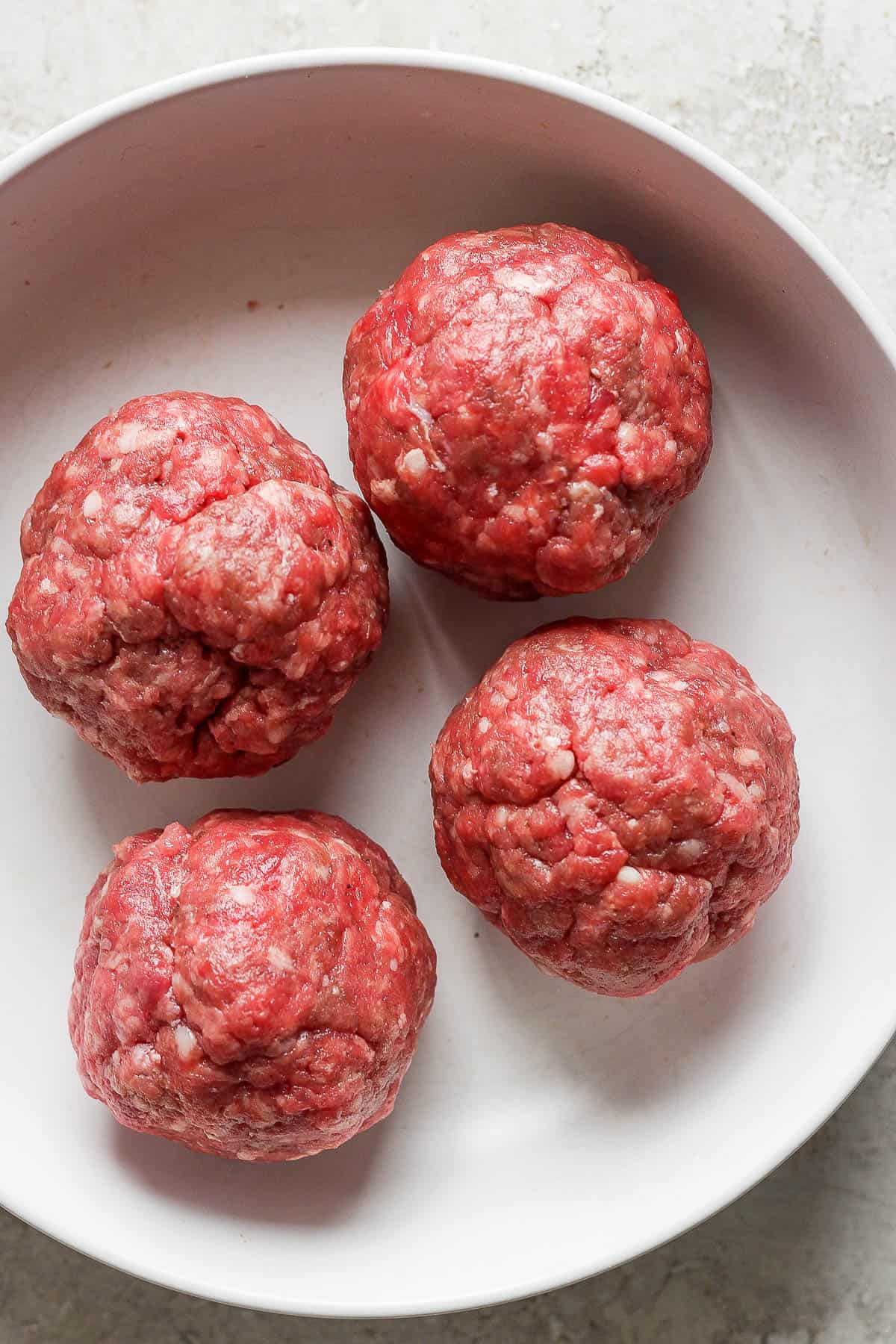 Ground beef smash burger balls in a bowl before being cooked.