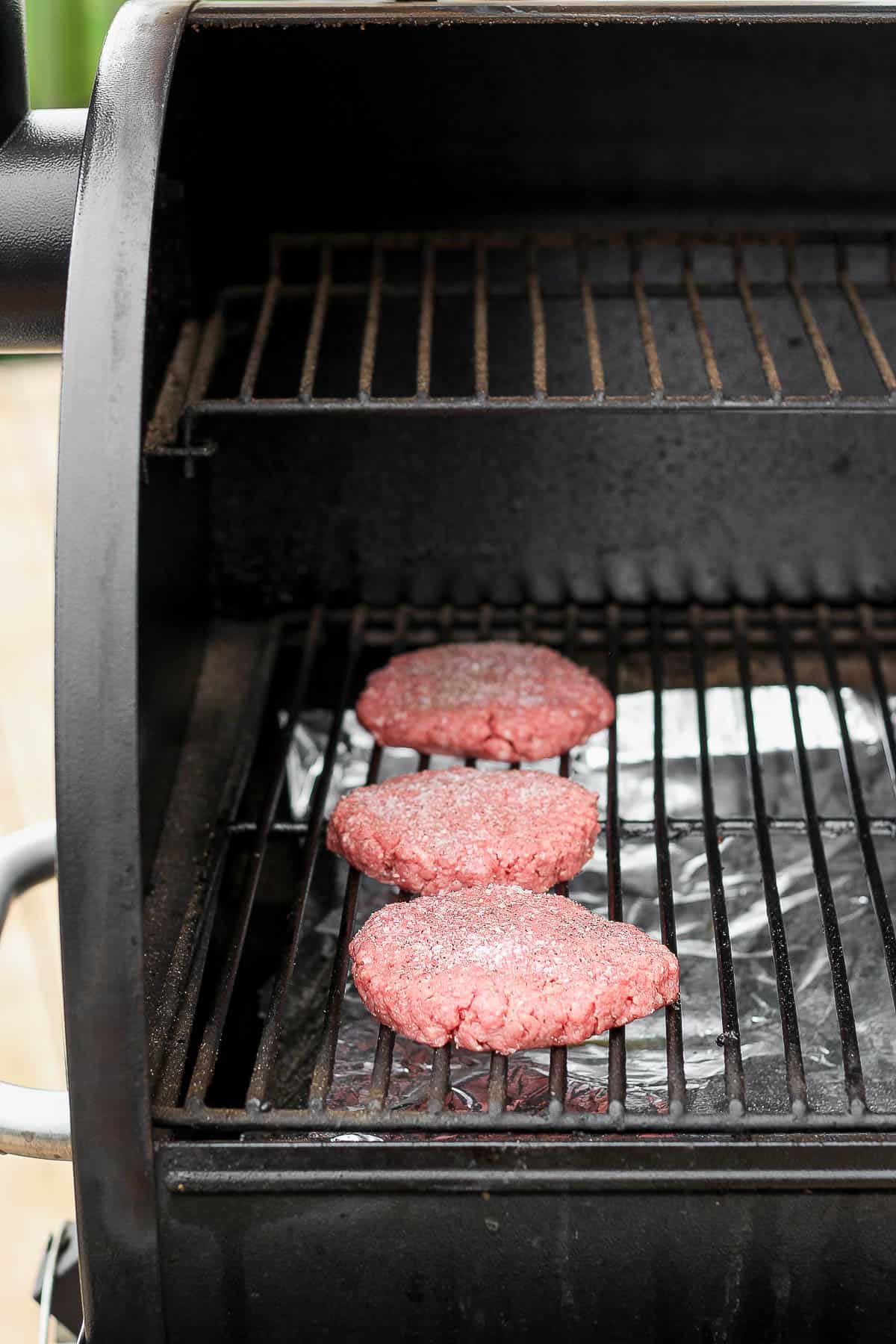 Three burgers on the smoker at the beginning of cooking.