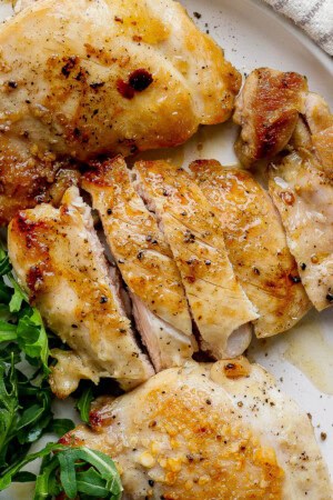 Three stove top chicken thighs on a plate next to some fresh greens.