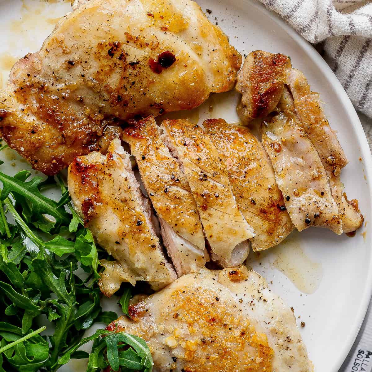 Three stove top chicken thighs on a plate next to some fresh greens.