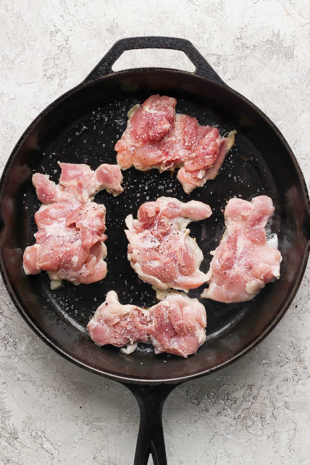 Stove top chicken thighs in a cast iron skillet before being flipped over.