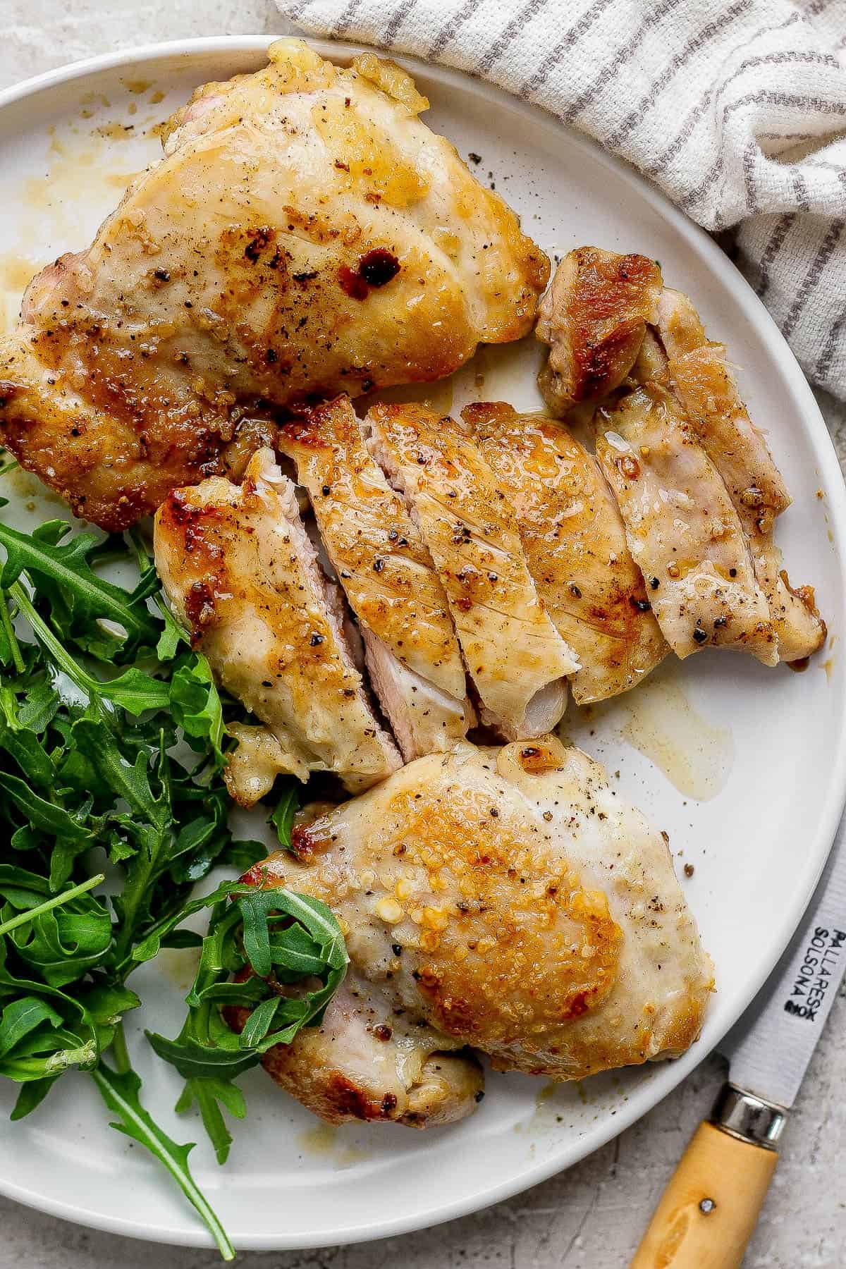 Three fully cooked stove top chicken thighs on a plate with fresh greens.