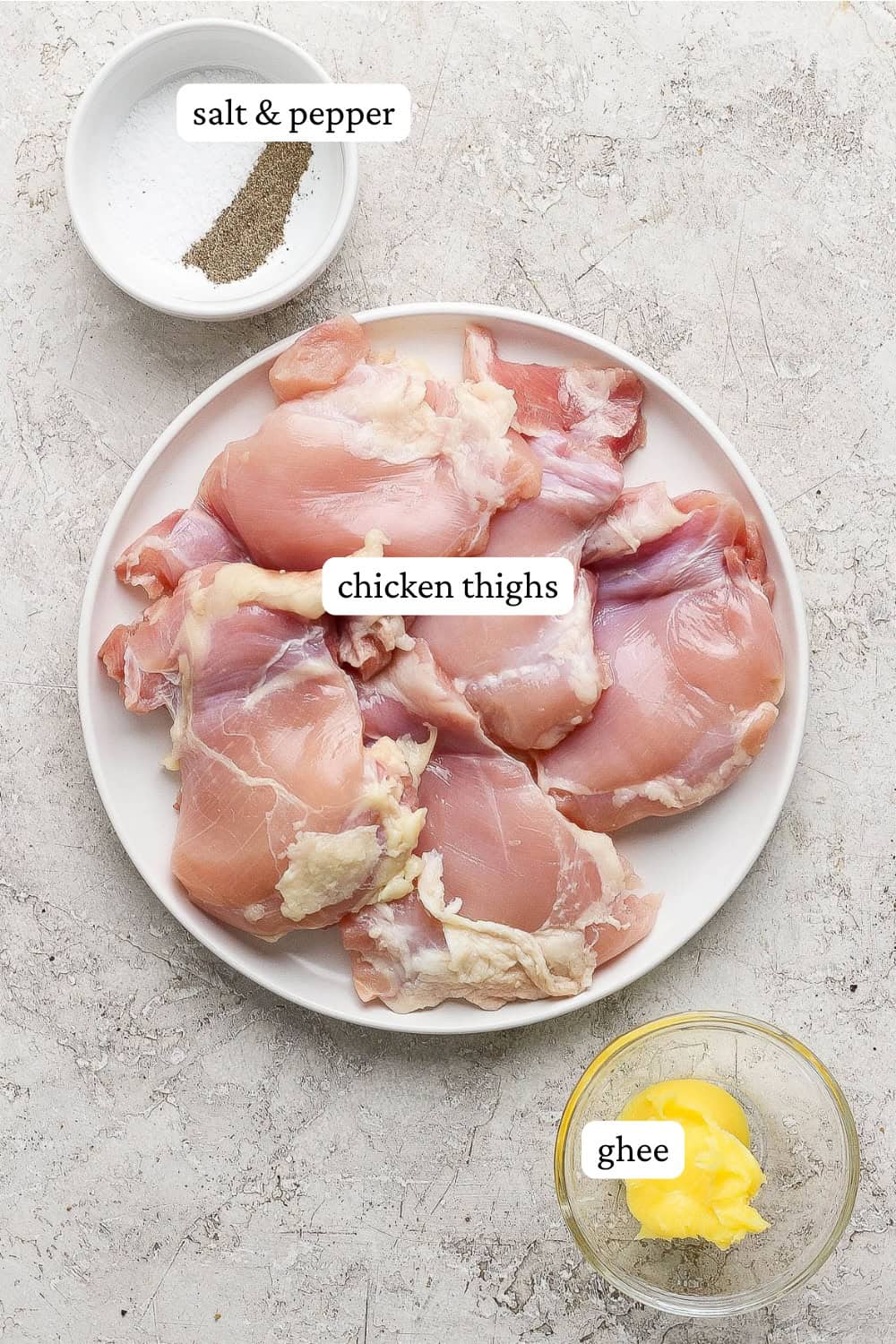 Raw chicken thighs on a plate next to small bowls of ghee, salt, and pepper with labels.