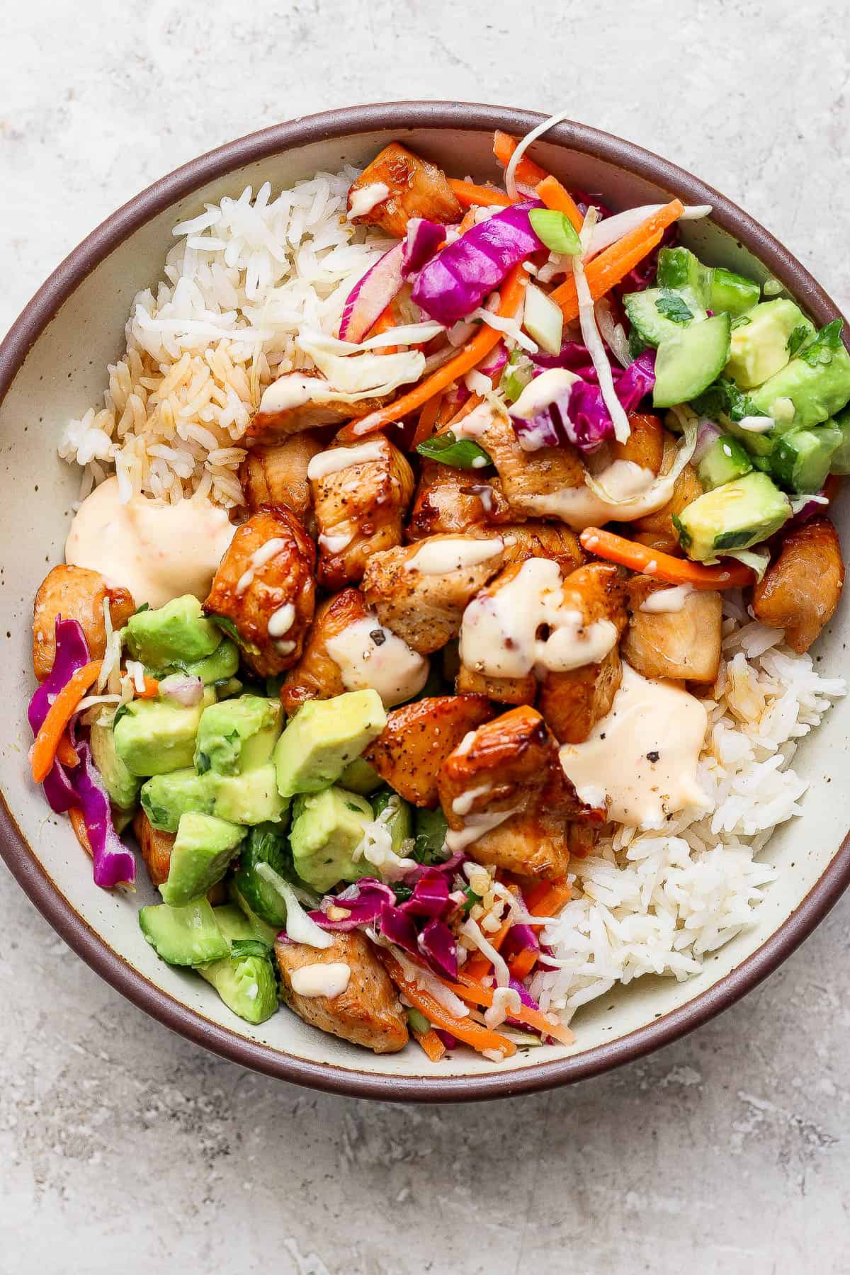 A fully assembled bang bang chicken rice bowl with sauce on top.