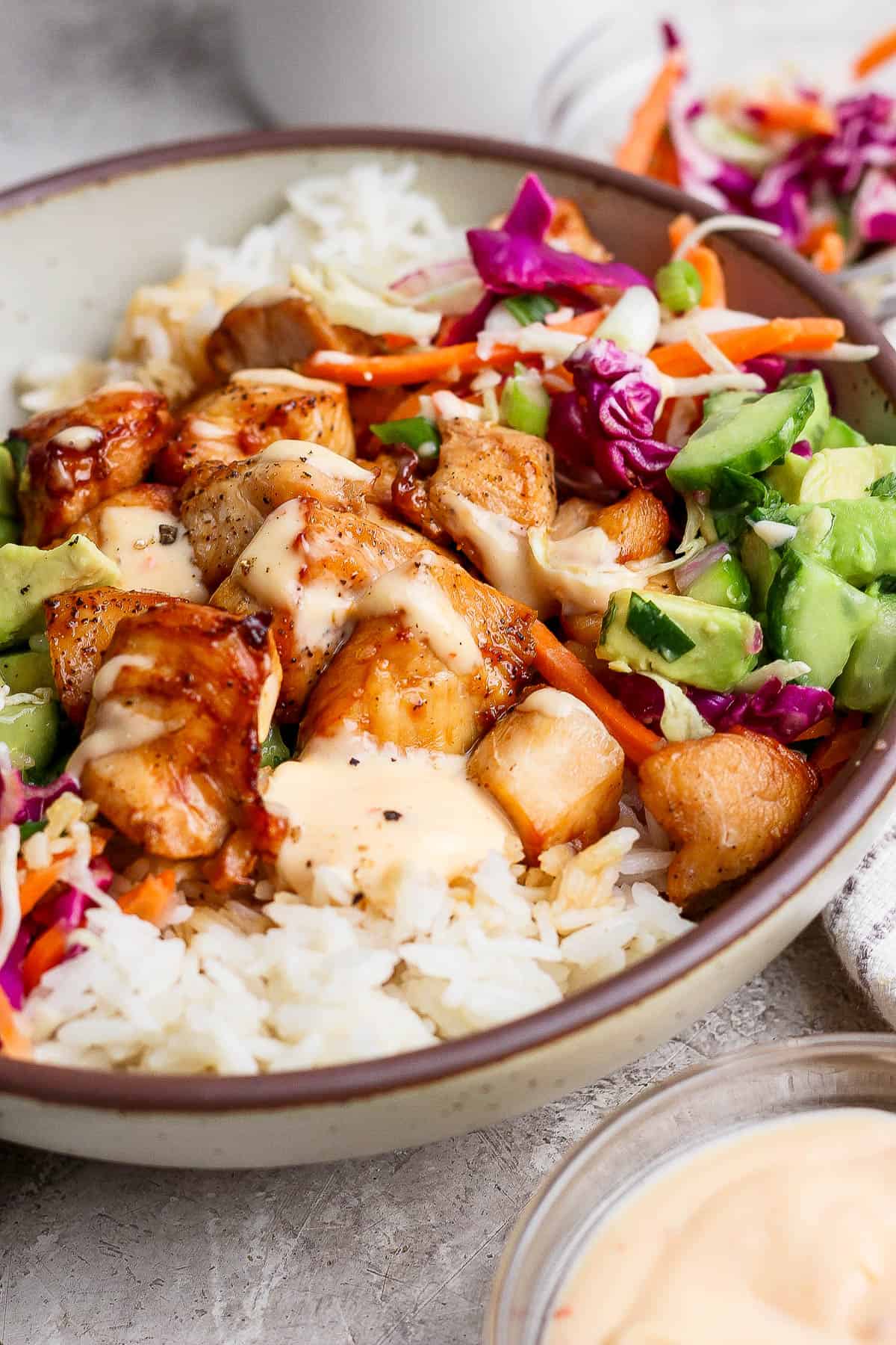 A bang bang chicken bowl with bang bang sauce on top next to a small bowl of shredded cabbage.