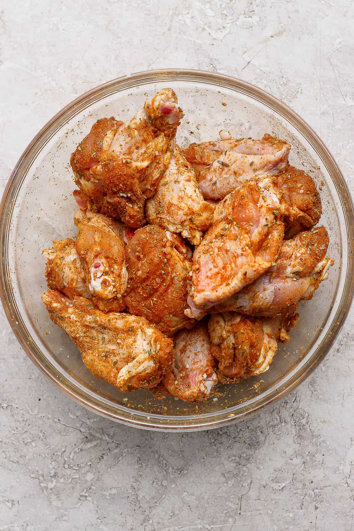 Blackstone chicken wings tossed in the dry rub in a glass bowl before cooking.