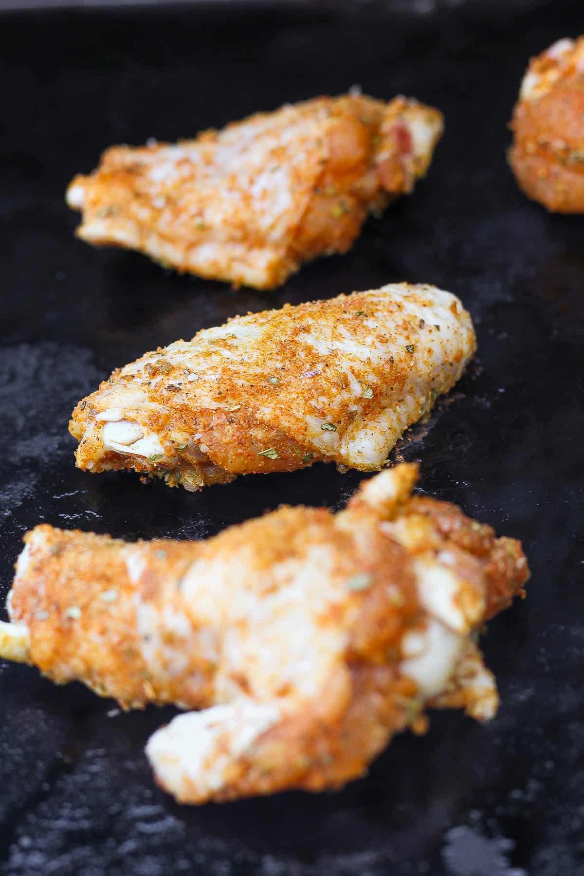 Chicken wings on the blackstone at the beginning of being cooked.