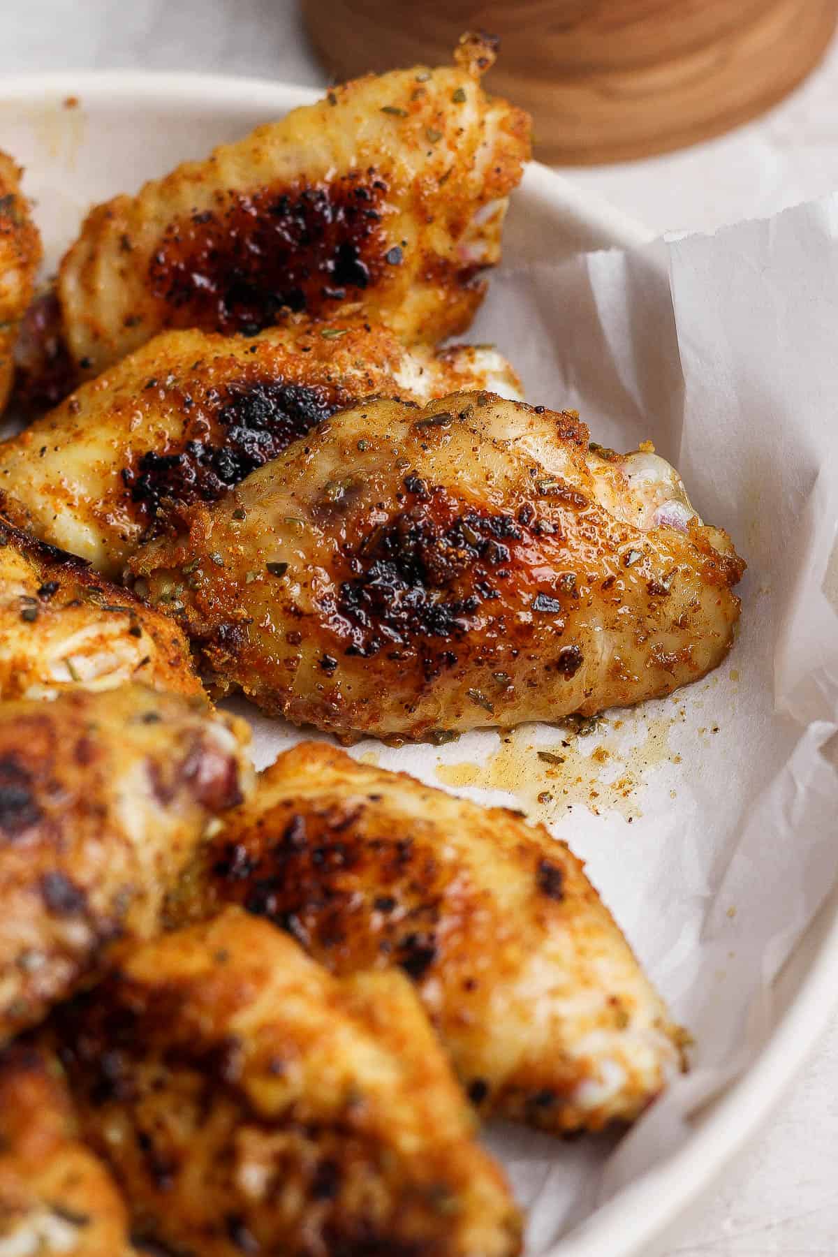Blackstone chicken wings resting in a shallow bowl with parchment paper.