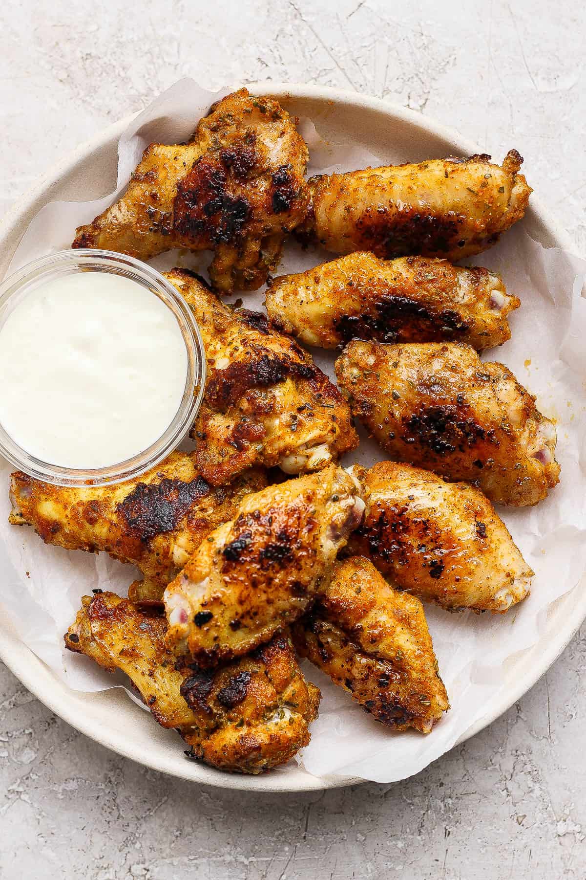 Blackstone chicken wings in a shallow bowl lined with parchment paper and a small dish of ranch dressing.