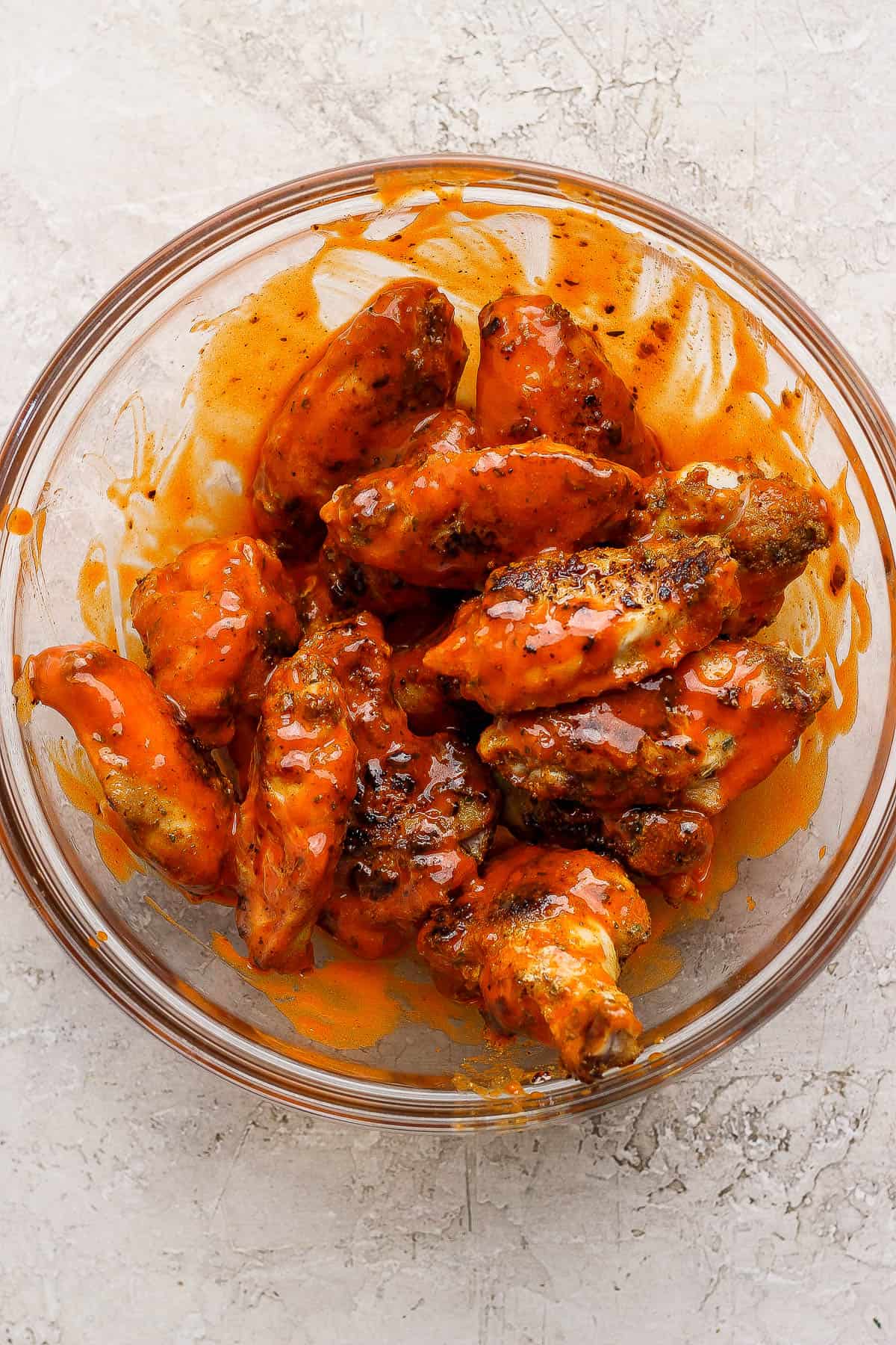 Blackstone chicken wings fully cooked and in a glass bowl with buffalo sauce.