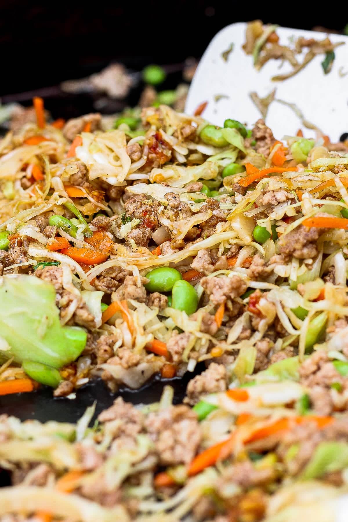 Blackstone egg roll in a bowl being tossed on the hot griddle with a large spatula.