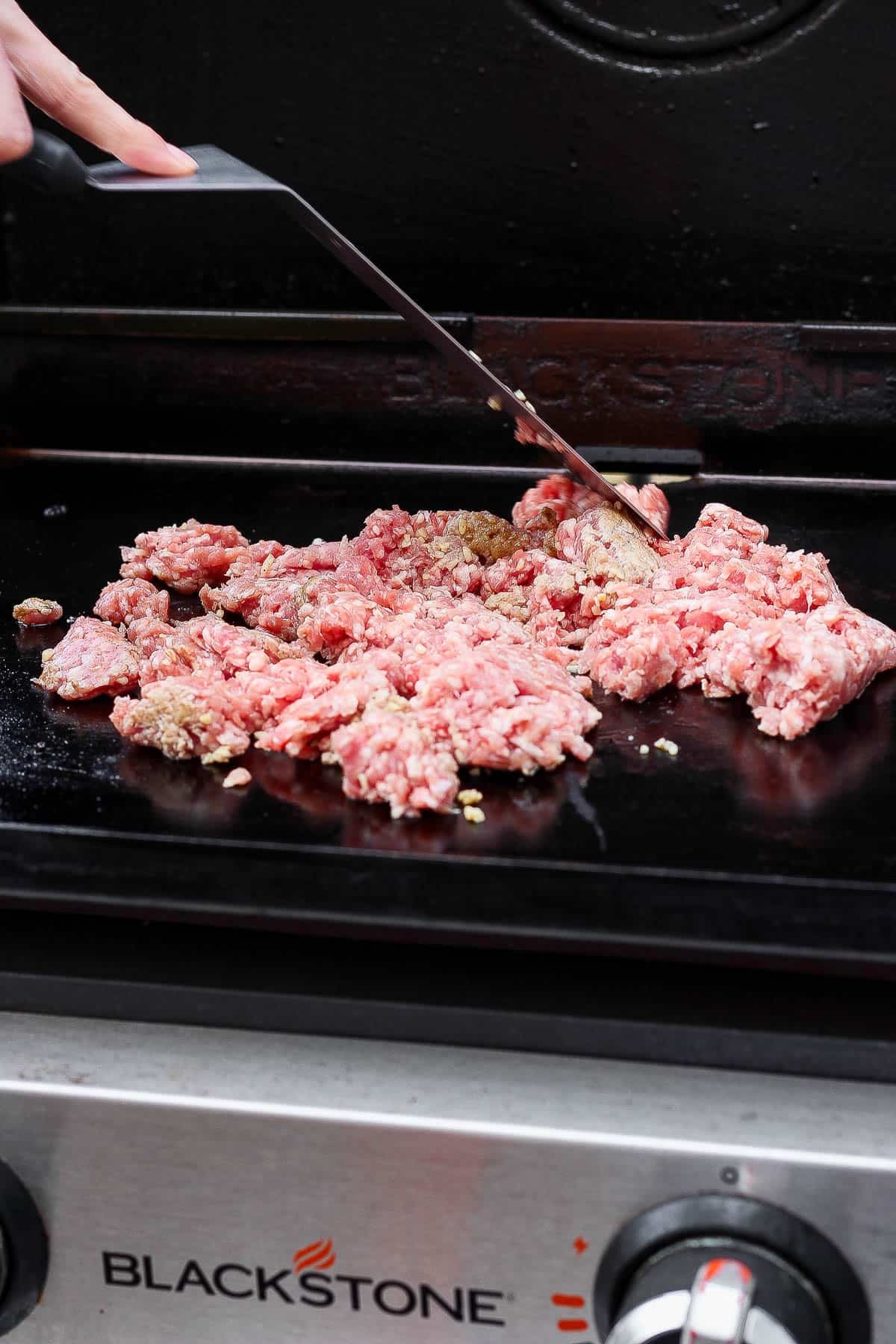 A large spatula breaking apart ground pork on a flattop griddle to make Blackstone egg roll in a bowl.