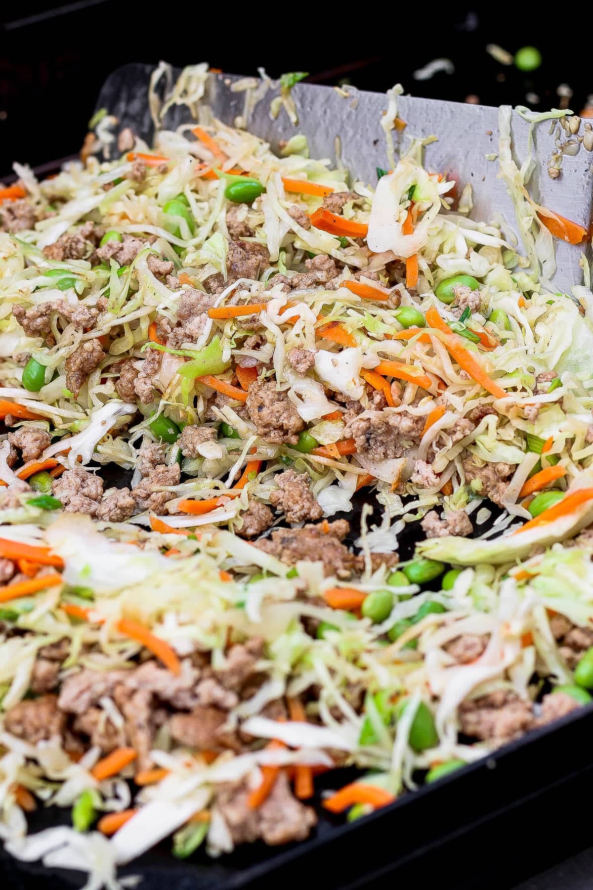 A large spatula tossing Blackstone egg roll in a bowl together on the griddle.