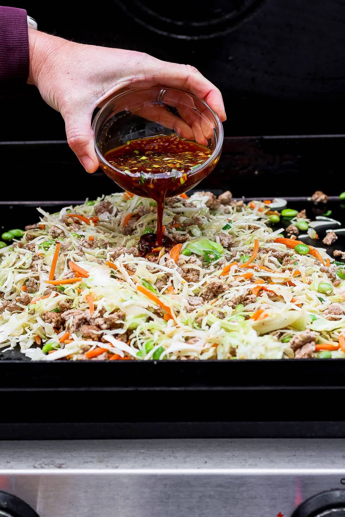 The sauce for Blackstone egg roll in a bowl being poured on the pork and coleslaw mixture.