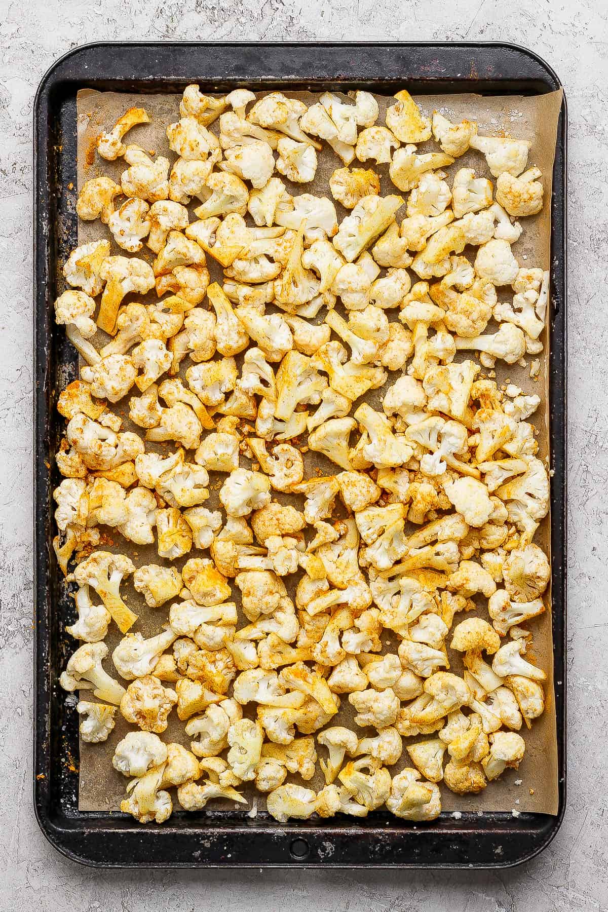 Cauliflower florets on a parchment-lined sheet pan after being tossed in olive oil and turmeric.