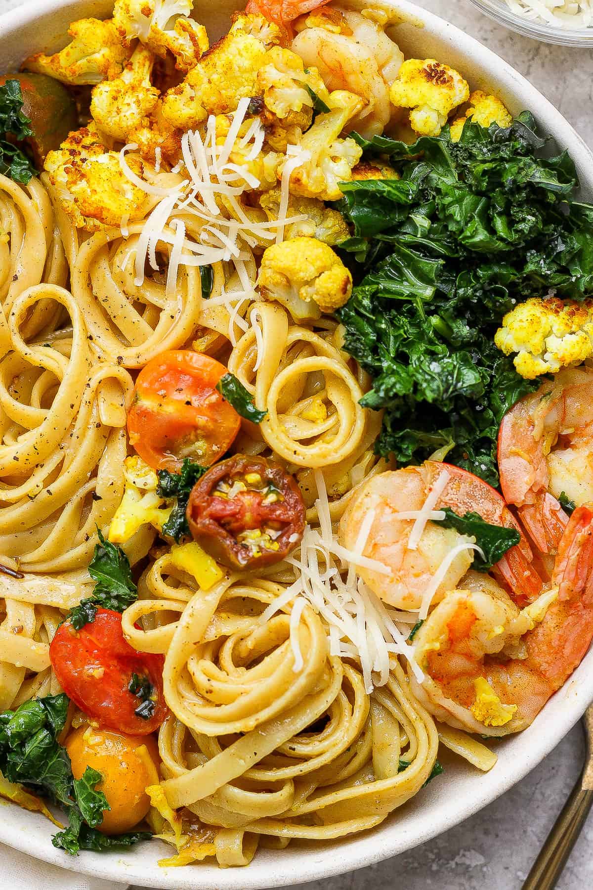Turmeric pasta with shrimp and cauliflower in a white bowl with parmesan cheese on top.