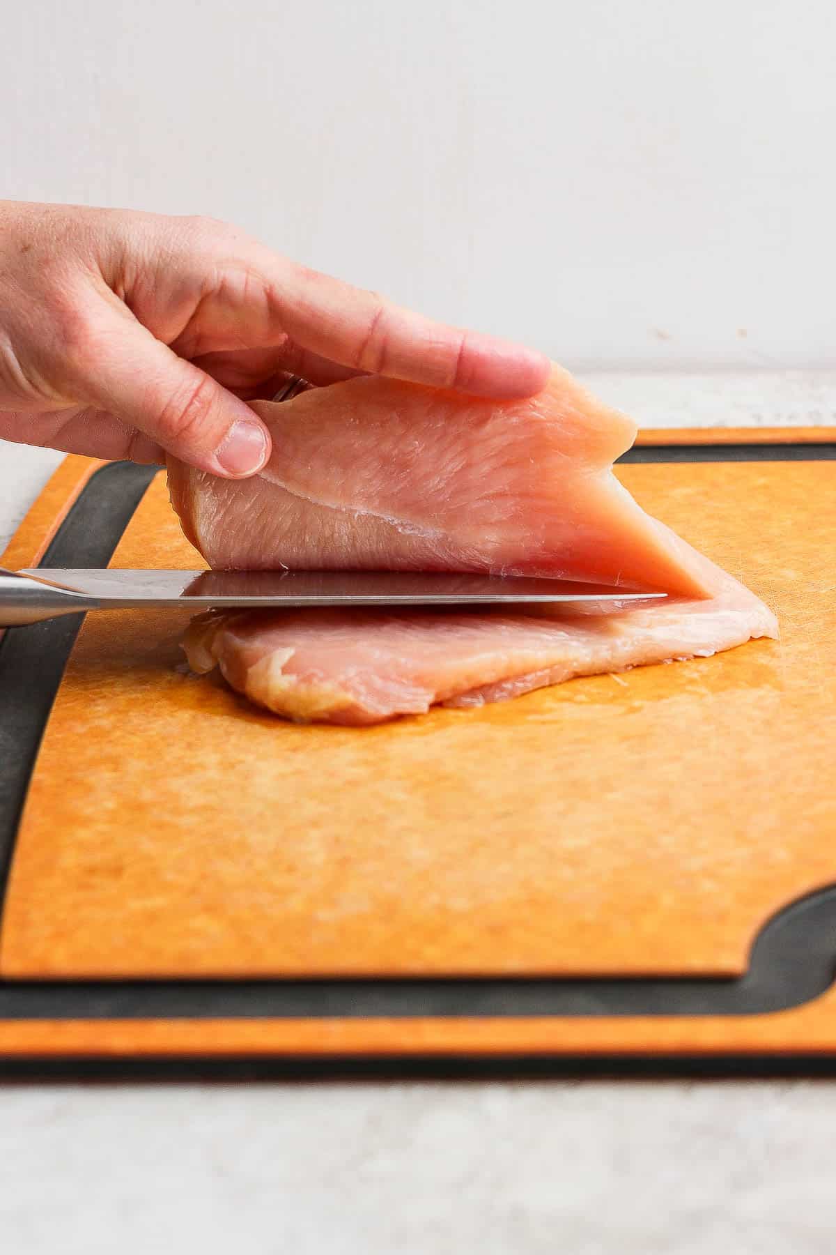 A chicken breast being cut into a cutlet on a cutting board to make chicken breasts on the Blackstone.
