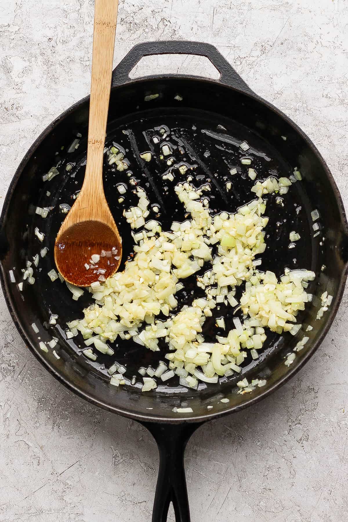 Sautéed onion and garlic for creamy tomato chicken thighs in a skillet.