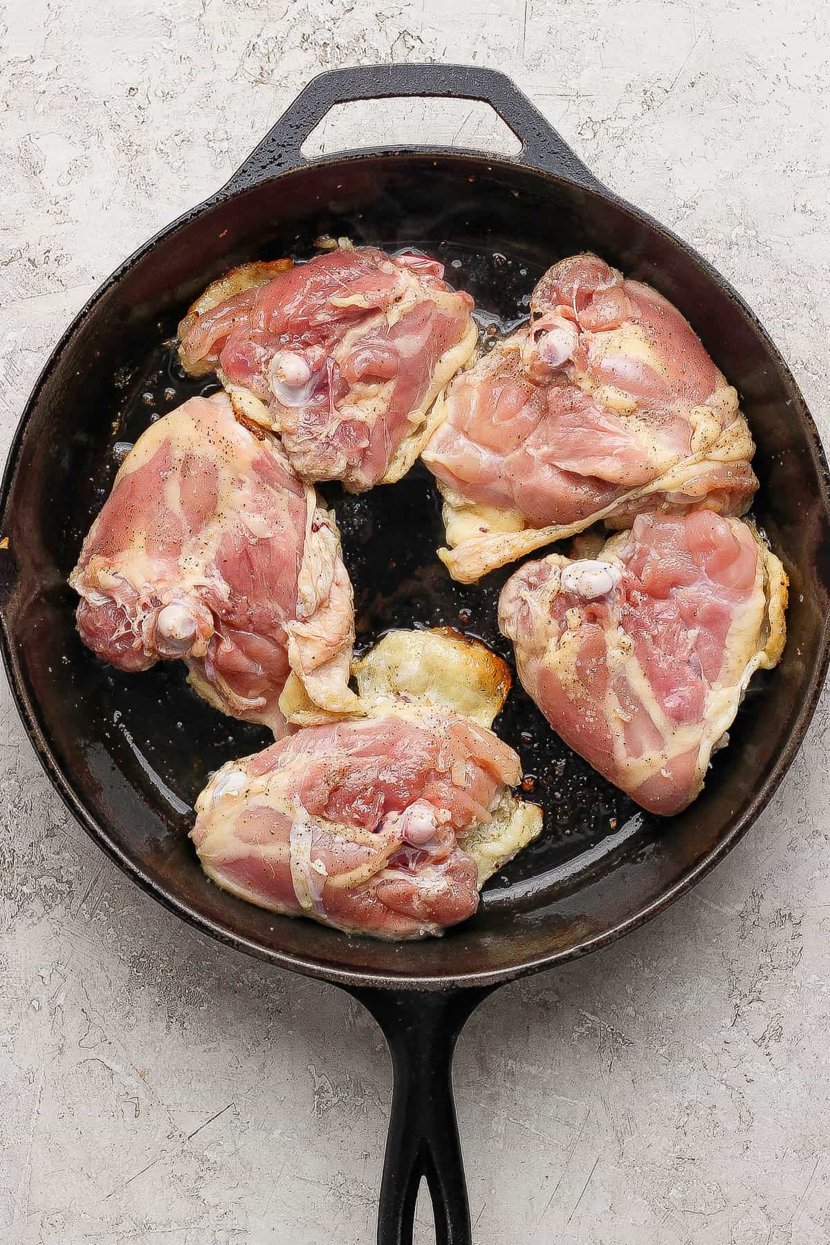 Bone-in chicken thighs searing with the skin-side down in a cast iron skillet.