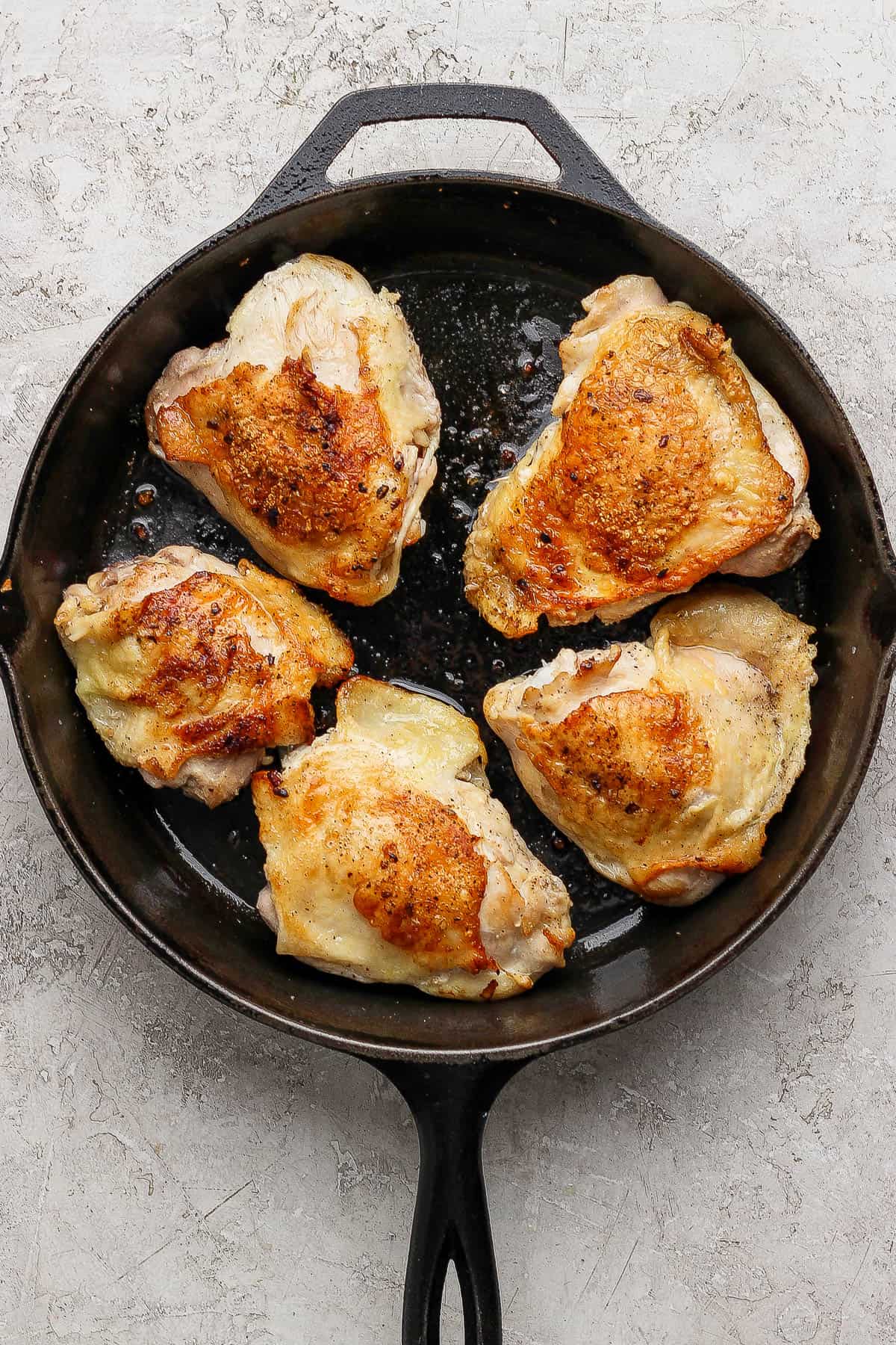 Bone-in chicken thighs searing in a cast iron skillet after being flipped and before adding the creamy tomato sauce.