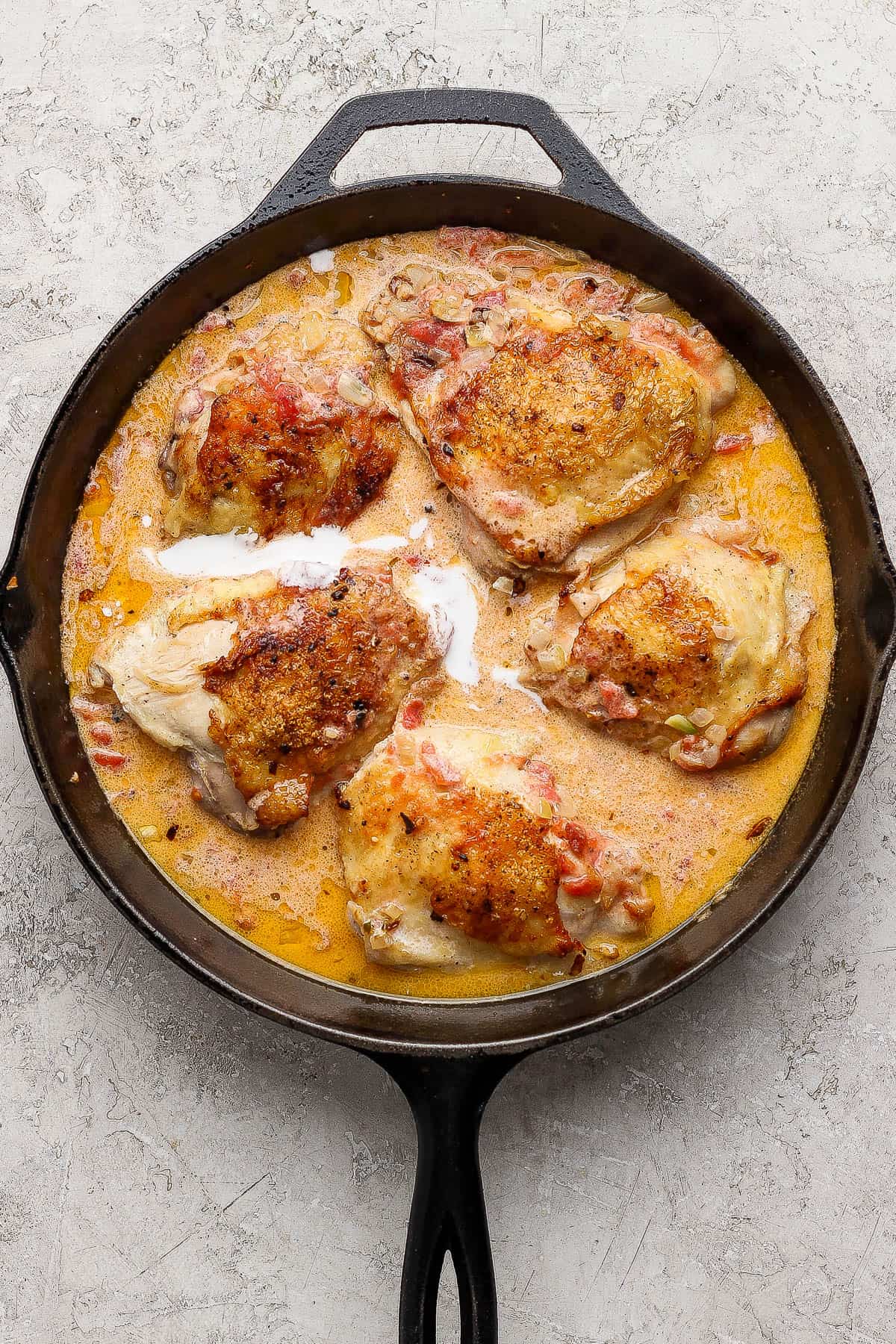 Coconut milk, tomatoes, and salt added to the pan with chicken thighs to make creamy tomato chicken thighs.