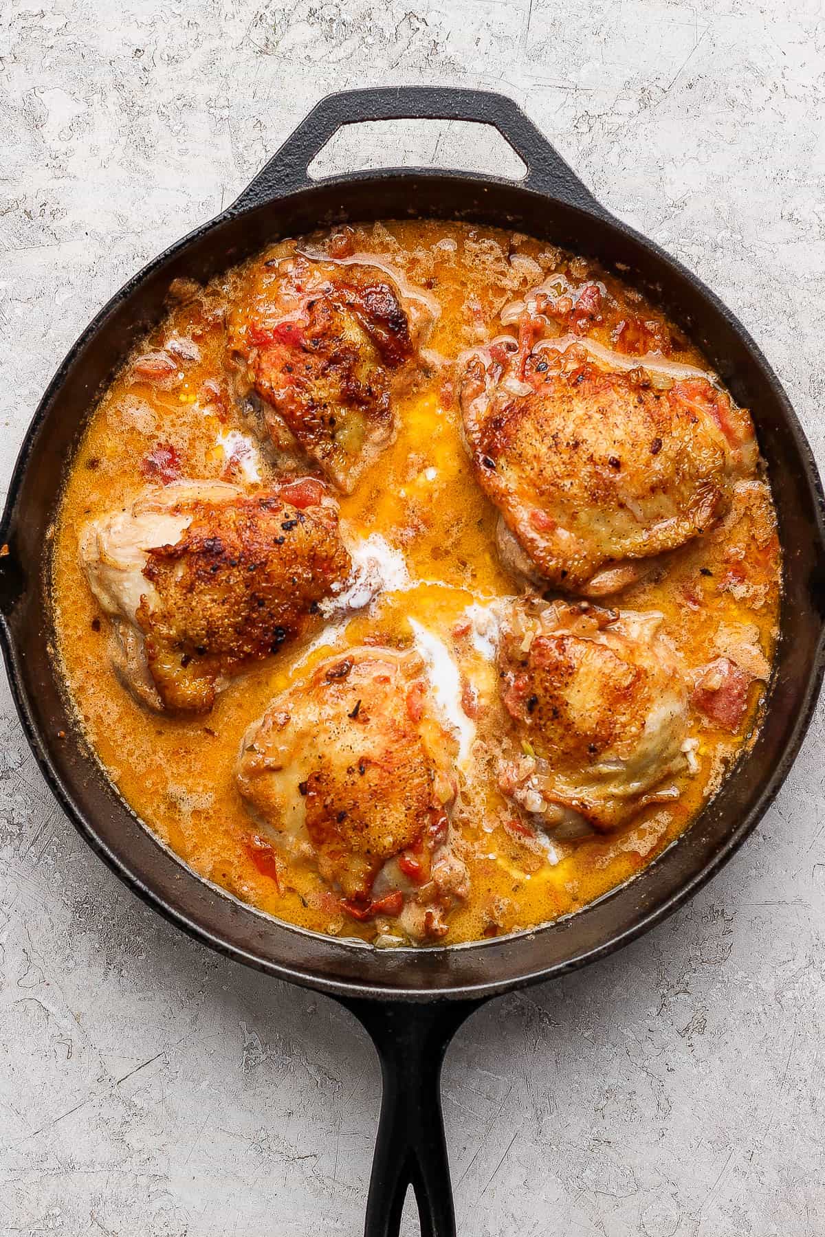 Creamy tomato chicken thighs in a cast iron skillet after simmering.