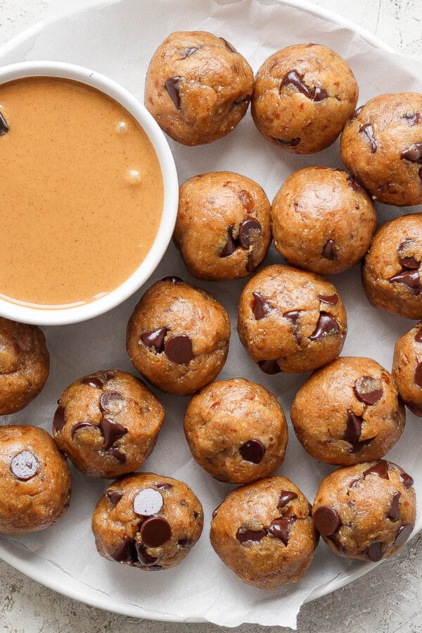 A plate filled with homemade chocolate chip cooke dough bites with a bowl of peanut butter with a spoon sticking out.