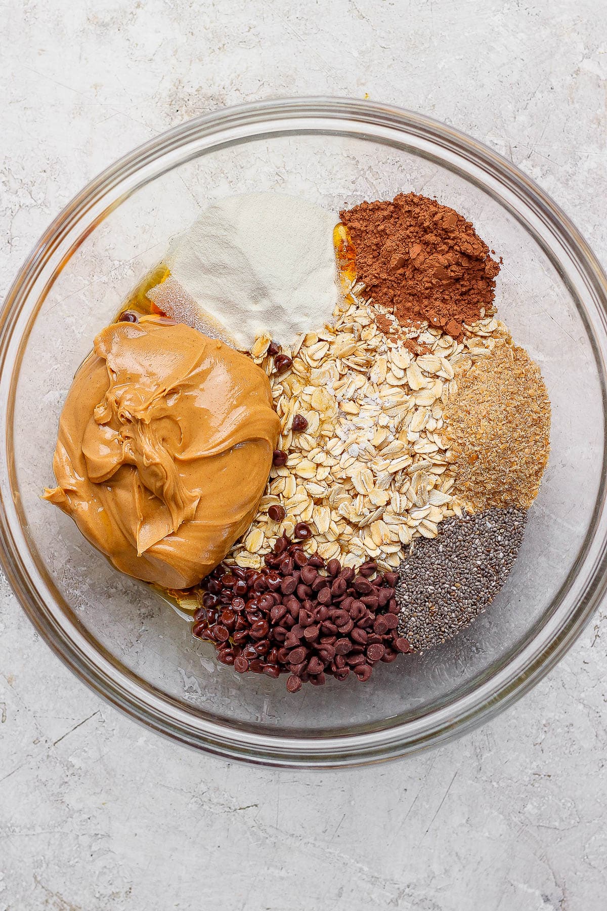 Ingredients for chocolate peanut butter energy balls separated in a large glass bowl.