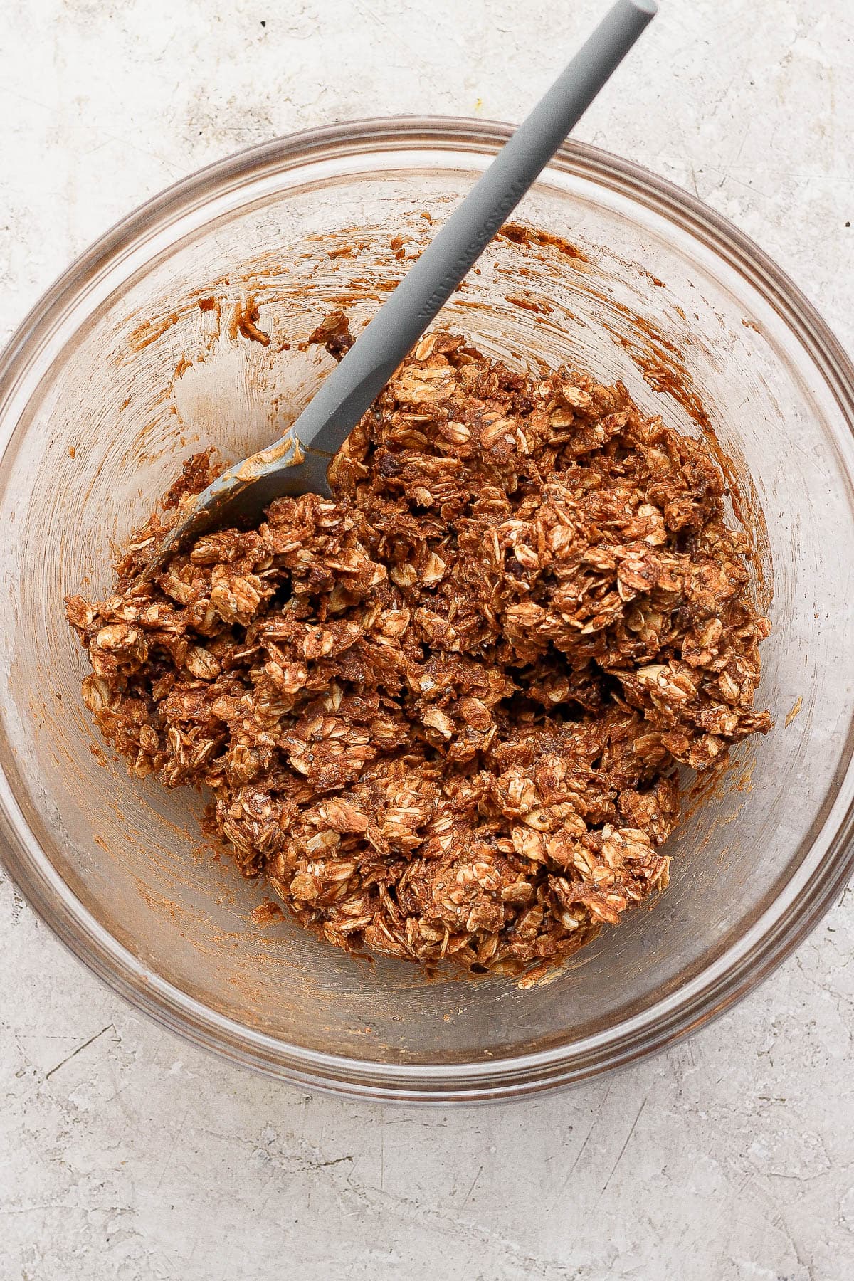 Ingredients for chocolate peanut butter energy balls mixed together in a glass bowl with a spatula.