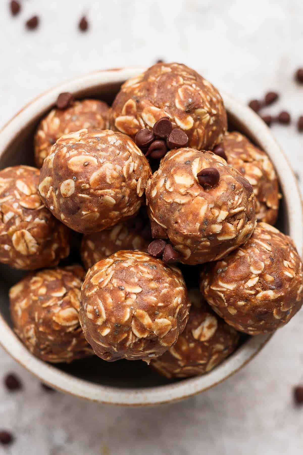 A bowl full of chocolate peanut butter energy balls with some chocolate chips sprinkled around it.