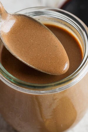 A jar of homemade creamy balsamic dressing with a spoon lifting some out.