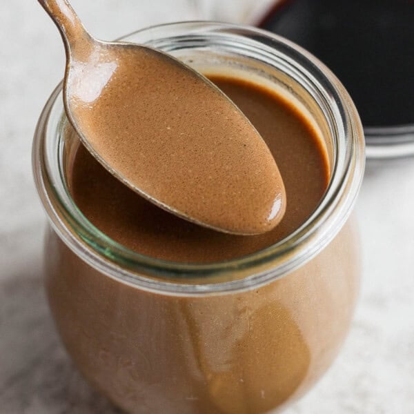 A jar of homemade creamy balsamic dressing with a spoon lifting some out.