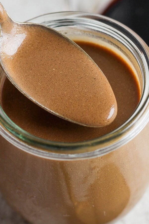 A jar of homemade creamy balsamic dressing with a spoon lifting some out.