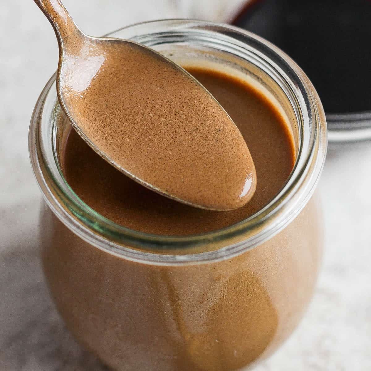 A jar of homemade creamy balsamic dressing with a spoon lifting some out.