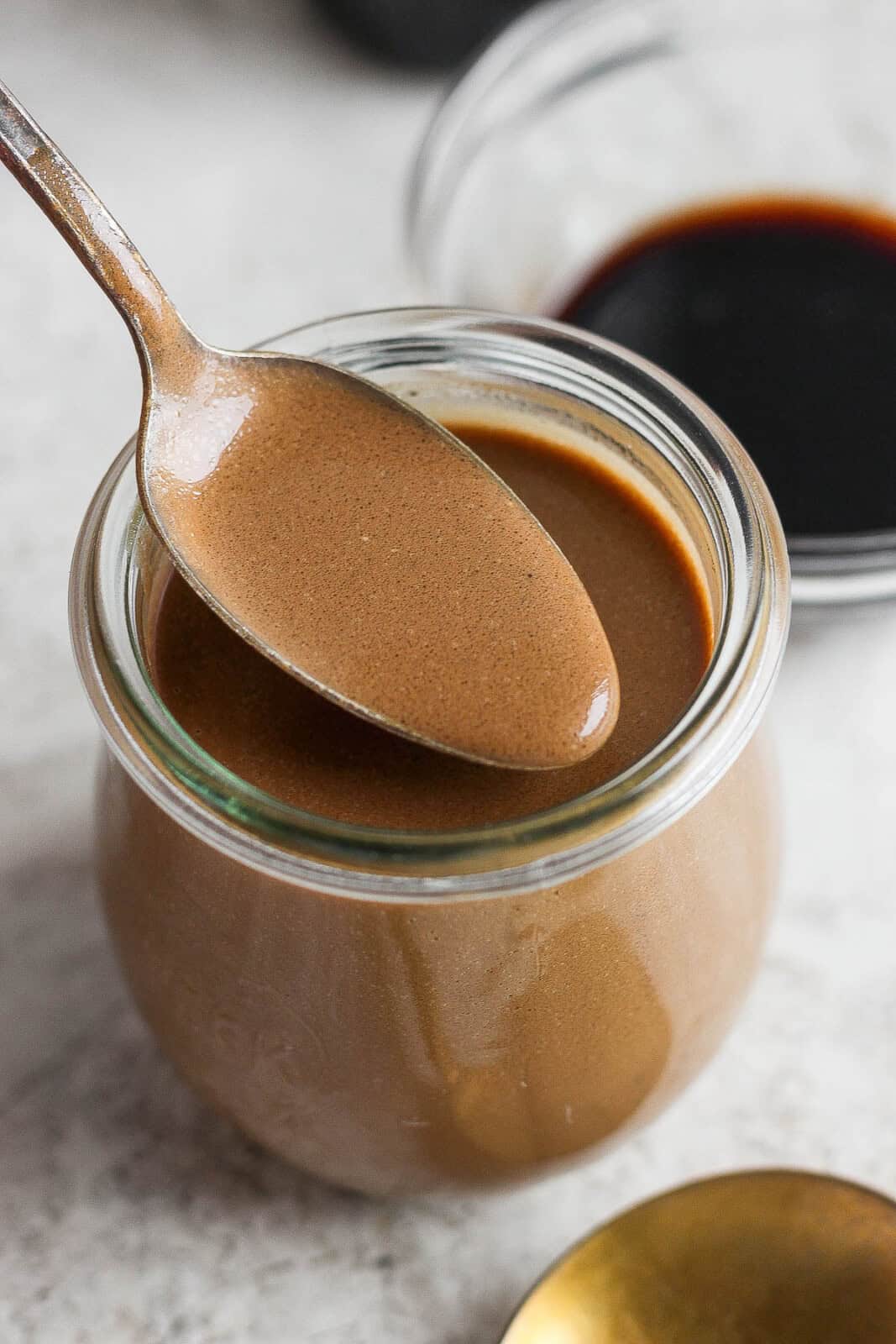 A jar of homemade creamy balsamic dressing with a spoon lifting some out. 