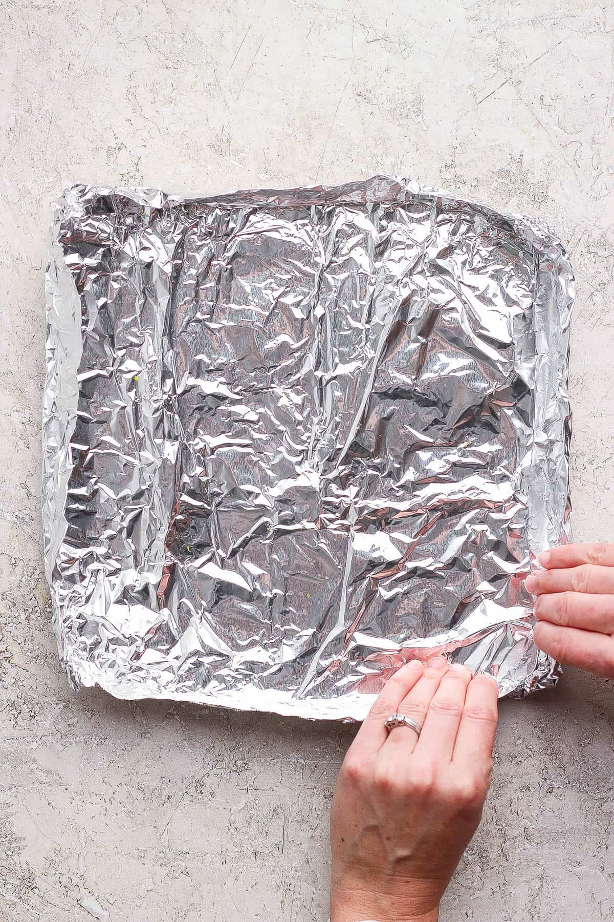 Two hands forming aluminum foil into a foil boat to hold grilled asparagus.