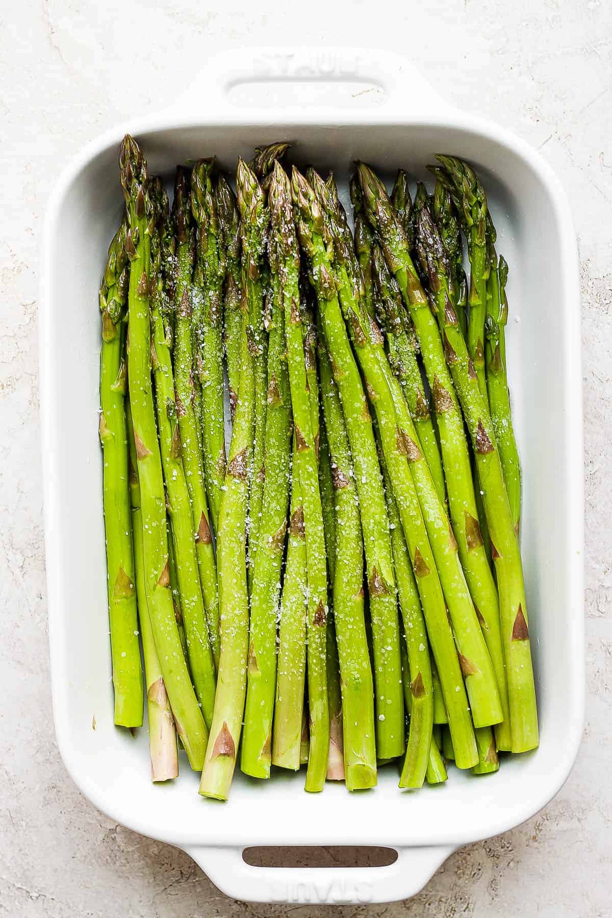 Fresh asparagus stalks seasoned with salt and pepper before going on the grill.