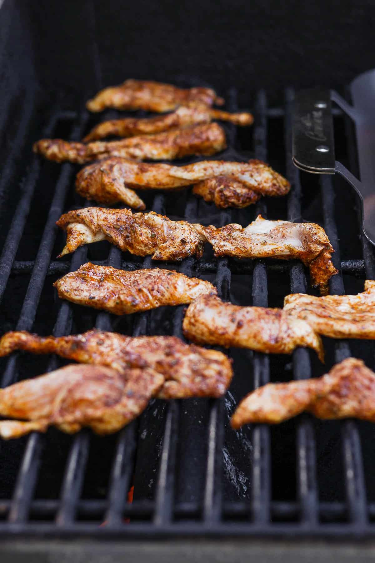 Fajita chicken strips cooking on a hot grill.