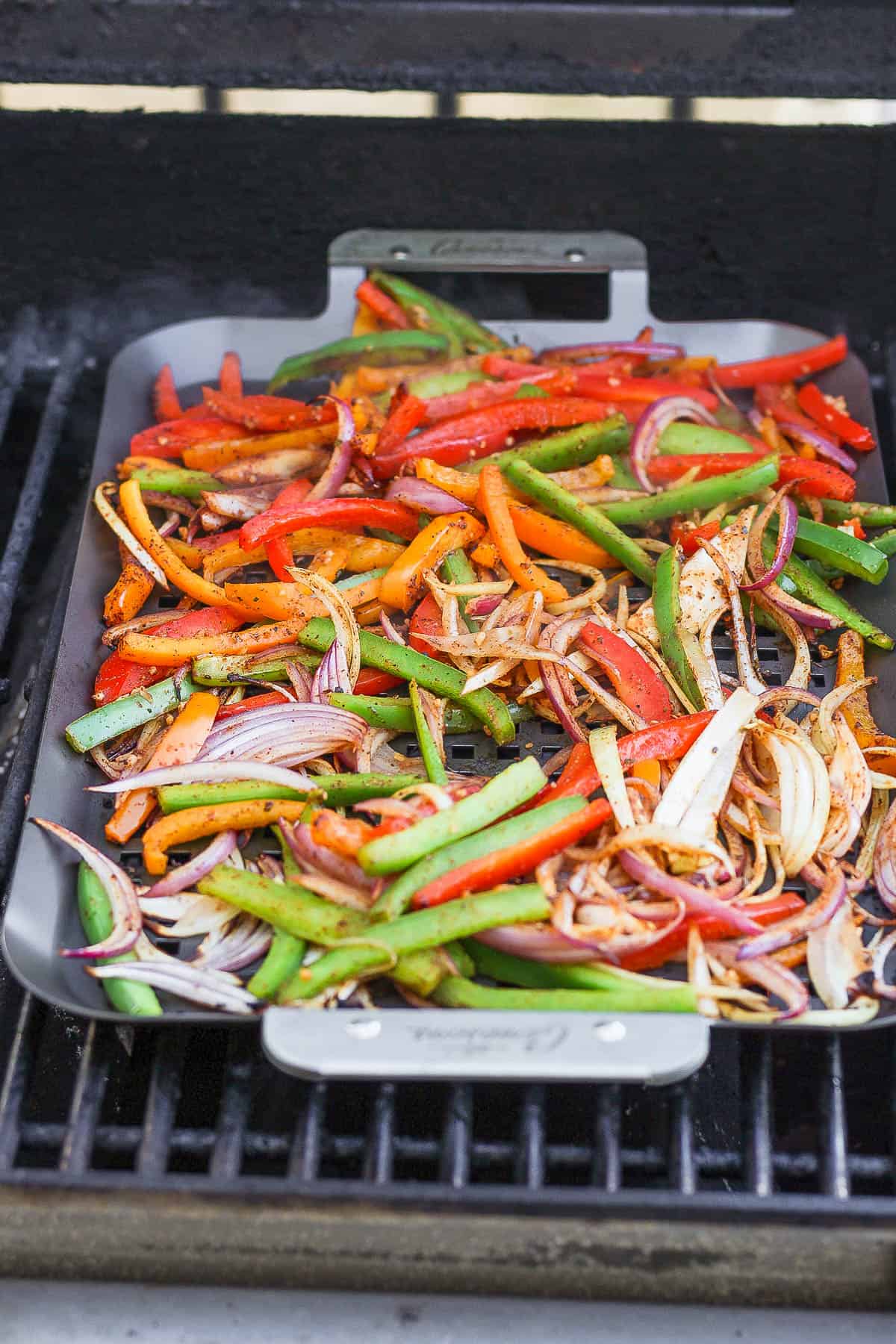 Fajita veggies cooking on a grill pan on the grill for grilled chicken fajitas.