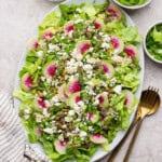 Spring salad with couscous and peas on a large serving platter next to gold silverware.