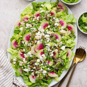 Spring salad with couscous and peas on a large serving platter next to gold silverware.